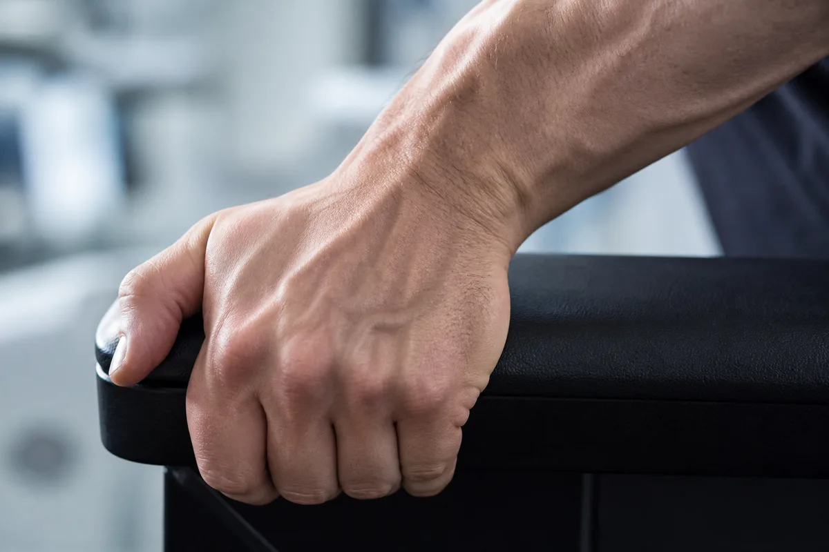 Gros plan sur une main aux doigts fermés sur le bord noir mat du fauteuil