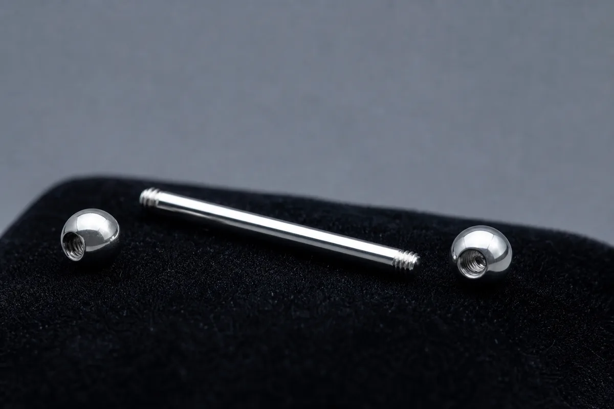 Macro sur une barre de piercing en titane poli et deux billes posées sur du velours noir